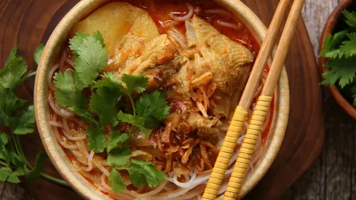 Semangkuk bihun kuah pedas dengan kuah merah berempah, lengkap dengan irisan cabai dan sayuran segar