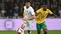 Bek Prancis William Saliba berebut bola dengan penyerang Afrika Selatan Bongokuhle Hlongwane dalam laga persahabatan di Stadion Pierre Mauroy, Rabu (30/3/2022) dinihari WIB. Timnas Prancis berpesta lima gol ke gawang Afrika Selatan. (DENIS CHARLET / AFP)