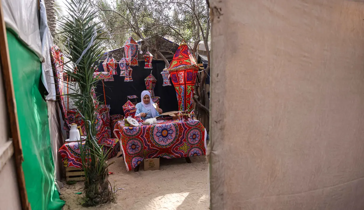 Sebagai informasi, fanous merupakan lentera tradisional berwarna-warni yang digunakan sebagai dekorasi khas untuk merayakan bulan suci Ramadan. Tampak dalam foto, Rehan Hazem Sharab, seorang pengungsi Palestina berusia 32 tahun, membuat lampion buatan tangan dari kotak-kotak bantuan yang tersisa sebagai persiapan menyambut bulan suci Ramadan yang dimulai pada 17 Februari, di luar tendanya di lingkungan Al-Mawasi, Khan Younis, di Jalur Gaza selatan pada Sabtu 7 Februari 2026. (Bashar Taleb/AFP)
