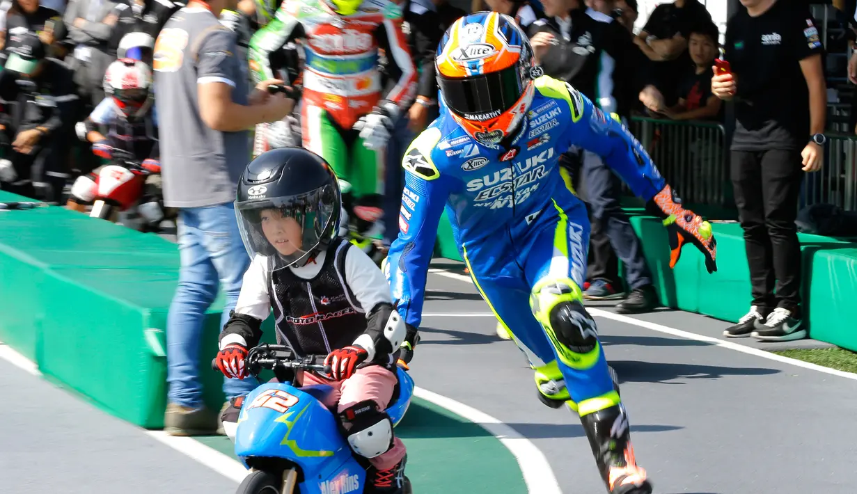 Pembalap MotoGP Alex Rins membantu seorang anak laki-laki mengendarai motor listrik mini saat acara jumpa pers jelang MotoGP Jepang di sirkuit Twin Ring Motegi, Jepang (12/10). (AP Photo / Shizuo Kambayashi)