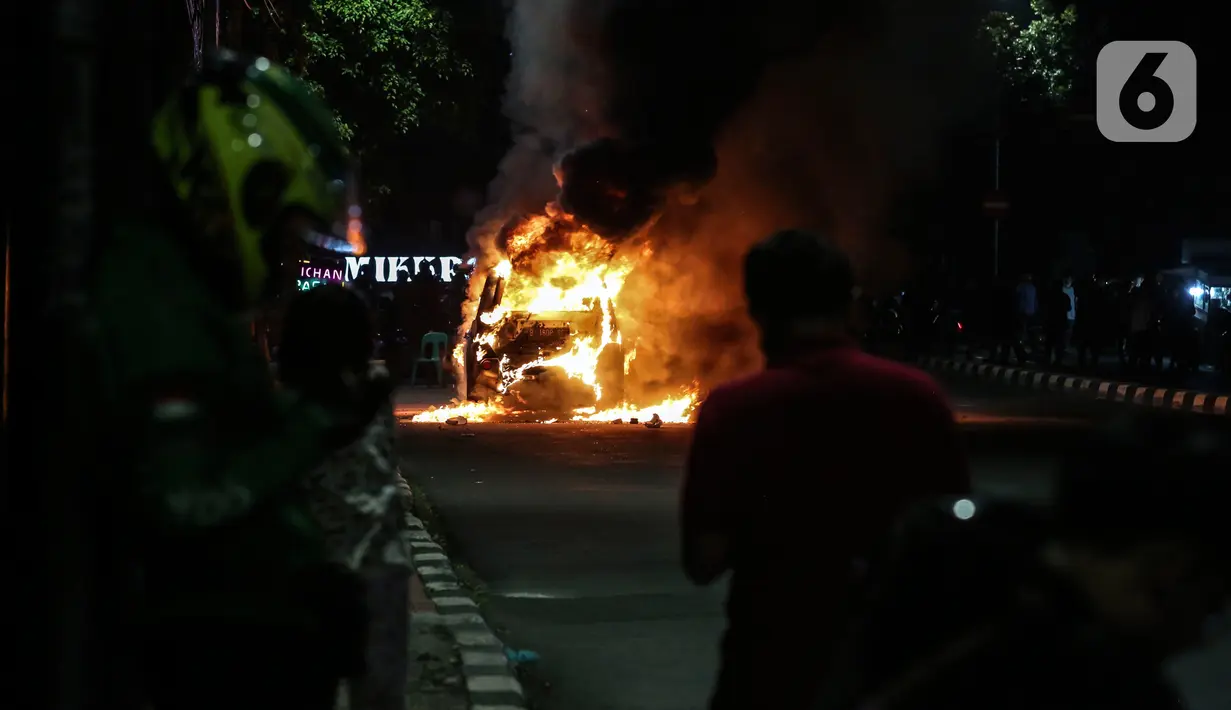 Warga menyaksikan sebuah mobil terbakar di Jalan Asia Afrika, Jakarta, Kamis (18/3/2021) dinihari. Api yang awalnya kecil akhirnya membesar hingga menghanguskan seluruh bagian mobil. (Liputan6.com/Johan Tallo)