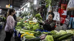 Pedangang melayani pelanggan di warung sayur di Hong Kong (1/3/2023). Hong Kong menjadi salah satu tempat terakhir di dunia yang masih menerapkan aturan masker. (AFP/Isaac Lawrence)