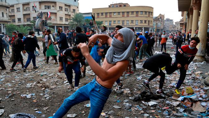 Demonstran antipemerintah melemparkan batu arah pasukan keamanan saat bentrok di Rasheed Street, Baghdad, Irak, Kamis (28/11/2019). Sebanyak 27 demonstran antipemerintah tewas ditembak mati oleh pasukan keamanan Irak dalam sehari. (AP Photo/Khalid Mohammed)