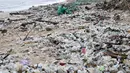 Seorang pria mengumpulkan plastik dan sampah lainnya yang terdampar di pantai Kedonganan, Kabupaten Badung, Bali, pada Jumat 27 Desember 2024. (SONNY TUMBELAKA/AFP)