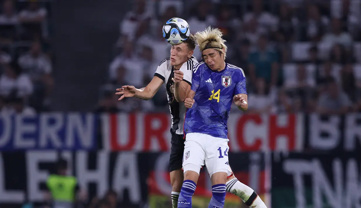 Pemain Timnas Jepang, Junya Ito (kanan), melakukan duel udara dengan pemain Timnas Jerman, Robin Gosens, dalam pertandingan persahabatan yang berlangsung di Volkswagen Arena, Wolfsburg, Minggu (10/9/2023). (AFP/Ronny Hartmann)