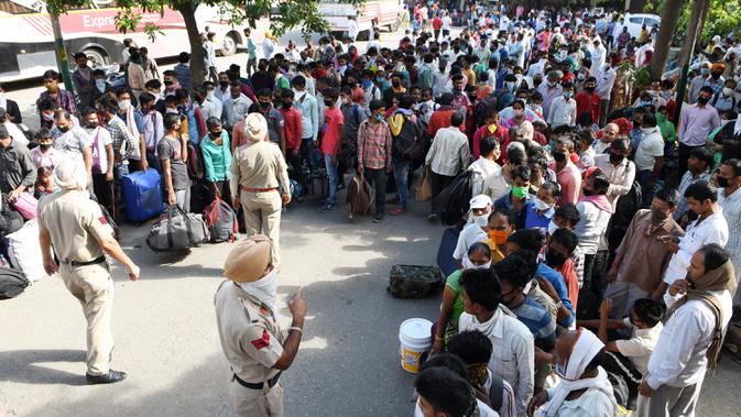 Personel polisi berjaga saat pekerja migran dan keluarga mereja antre menunggu pemeriksaan medis sebelum menaiki kereta untuk kembali ke kota asal mereka ke Jaunpur, negara bagian Uttar Pradesh, setelah pemerintah melonggarkan lockdown di Amritsar, India, Selasa (19/5/2020). (NARINDER NANU/AFP)