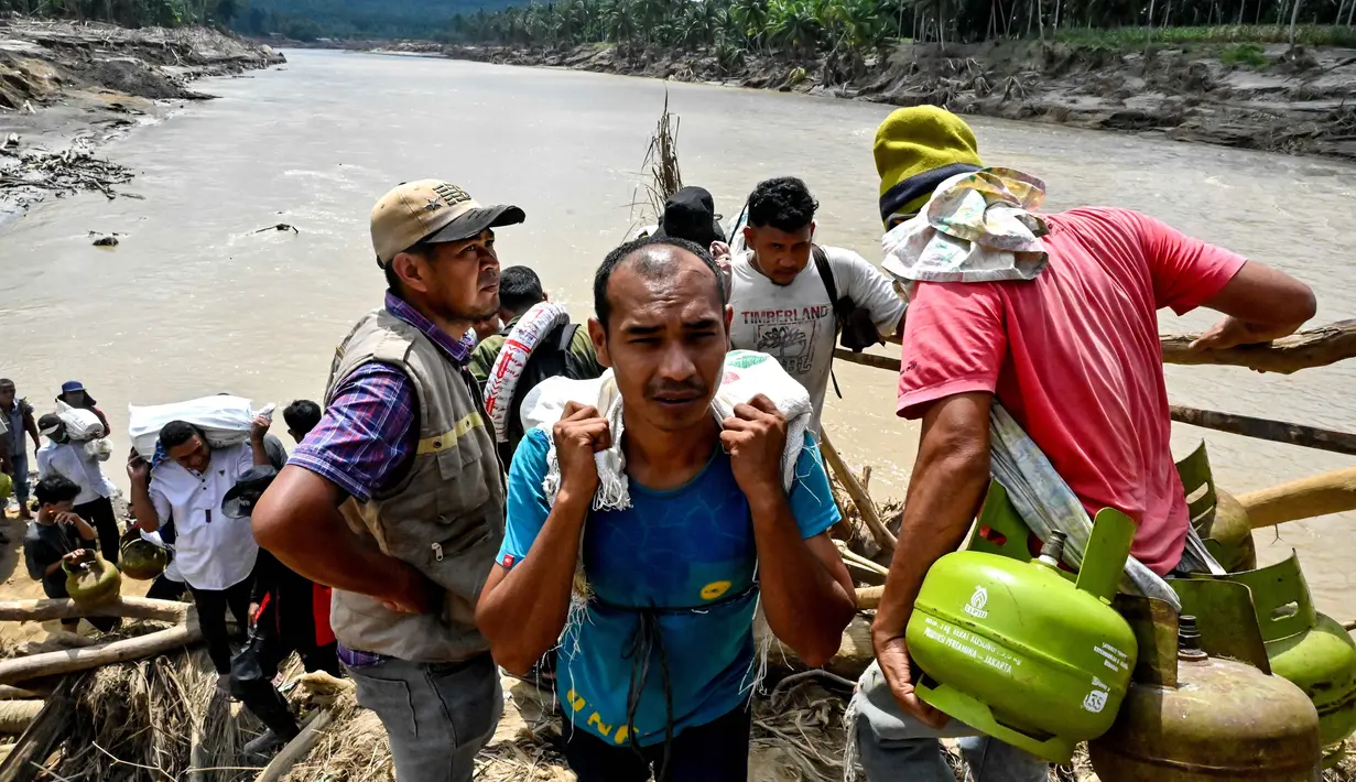 Tumpukan puing kayu menjadi solusi sementara sekaligus jalur alternatif bagi warga untuk melanjutkan aktivitas harian dan mengambil bantuan logistik. Tampak dalam foto, warga menyeberangi sungai di jembatan yang baru dibangun yang menghubungkan Aceh dan Provinsi Sumatera Utara setelah hancur akibat banjir bandang di Sungai Peusangan, Distrik Bireuen, Provinsi Aceh, Selasa 9 Desember 2025. (CHAIDEER MAHYUDDIN/AFP)