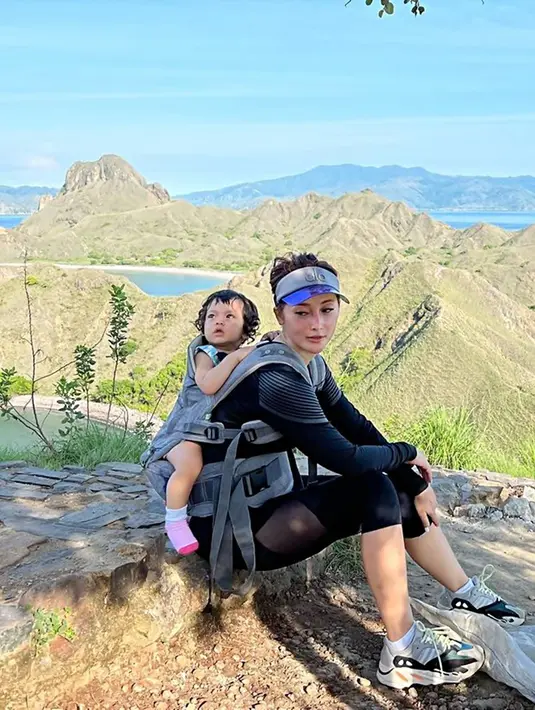 Liburan ke Labuan Bajo. Eva bersama suami dan anaknya ini menikmati indahnya pemandangan alam. Tampil sporty, Eva yang kini sudah berusia 36 tahun ini jalan-jalan sambil menggendong si kecil. (Liputan6.com/IG/@eva_anindita_zachrie)
