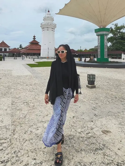 Atasan hitam model kaos itu dipadukan bawahan kain batik warna biru salur hitam. Dipadukan sandal Hermes hitamnya. [@wulanguritno]