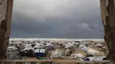 Badai musim dingin yang membawa angin kencang dan suhu ekstrem dilaporkan menghancurkan sejumlah tempat perlindungan. Tampak dalam foto, sebuah foto menunjukkan tenda-tenda penampungan keluarga-keluarga Palestina yang mengungsi, didirikan di sepanjang pantai Kota Gaza saat angin musim dingin yang kencang menerpa wilayah tersebut pada Selasa 13 Januari 2026. (Omar AL-QATTAA/AFP)