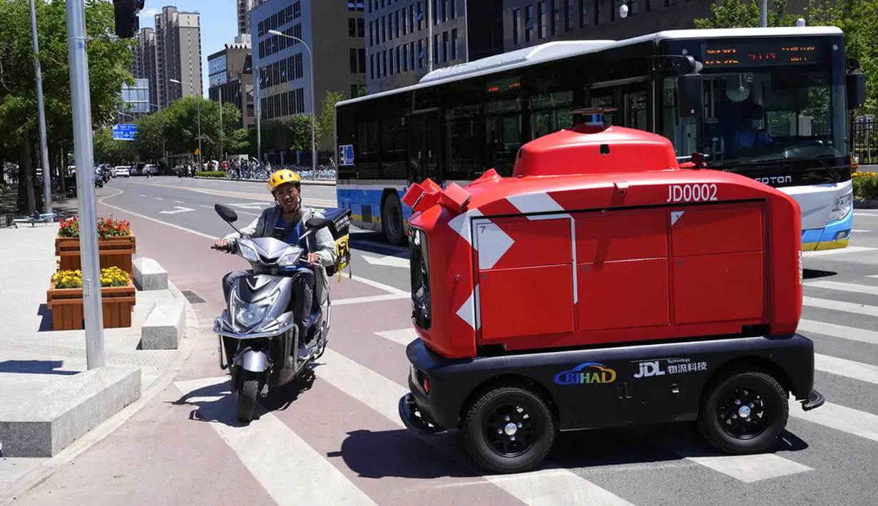 Seorang petugas pengiriman melewati kendaraan pengiriman otonom dari JD.com di jalanan Beijing, China, Jumat (28/5/2021). Anak perusahaan China JD.com, JD Logistics, diberi izin untuk menjalankan kendaraan di jalan terbuka yang ditentukan di tenggara Beijing. (AP Photo/Ng Han Guan)