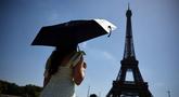Seseorang berlindung di bawah payung saat berjalan menuju Menara Eiffel di Paris ketika gelombang panas yang memecahkan rekor melanda sebagian besar Eropa Barat pada Kamis 28 Mei 2026. (SIMON WOHLFAHRT/AFP)