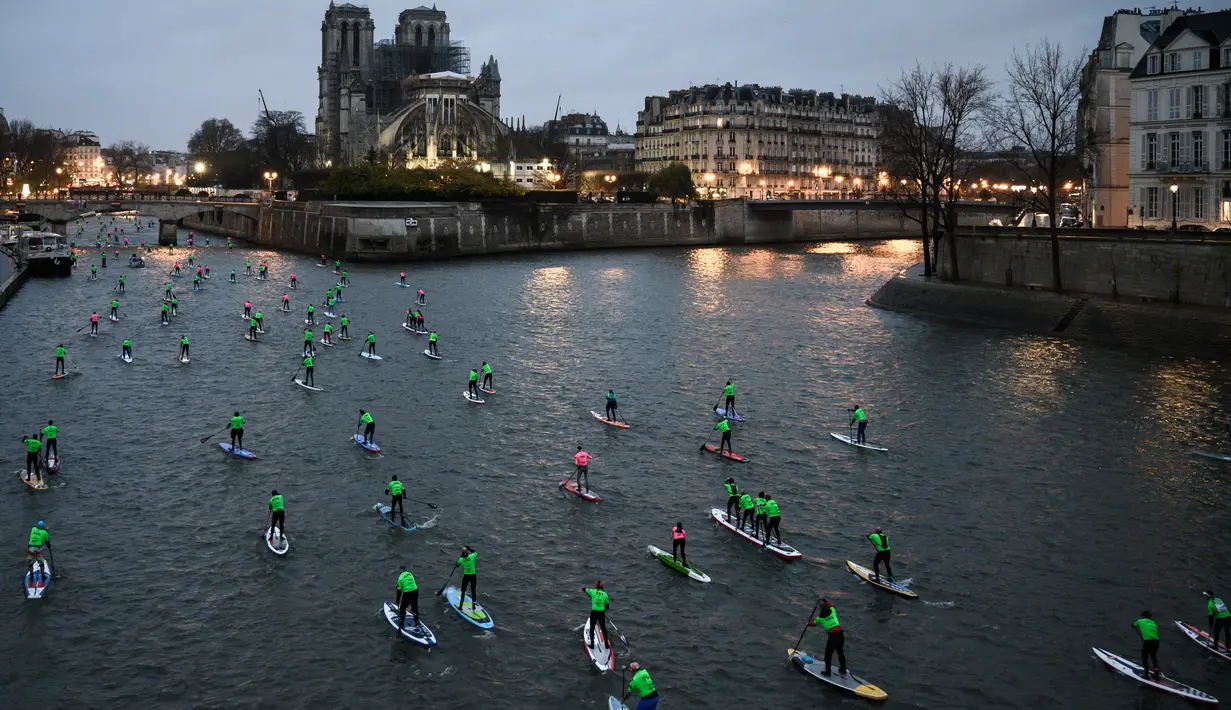 Para peserta Nautic Paddle Race atau lomba dayung sambil berdiri melintas dekat Katedral Notre-Dame di Paris, Minggu (8/12/2019). Sekitar 1000 pesaing ikut serta dalam lomba sejauh 11 kilometer menyeberangi sungai Seine dengan pemandangan kota Paris. (Photo by Olivier MORIN / AFP)