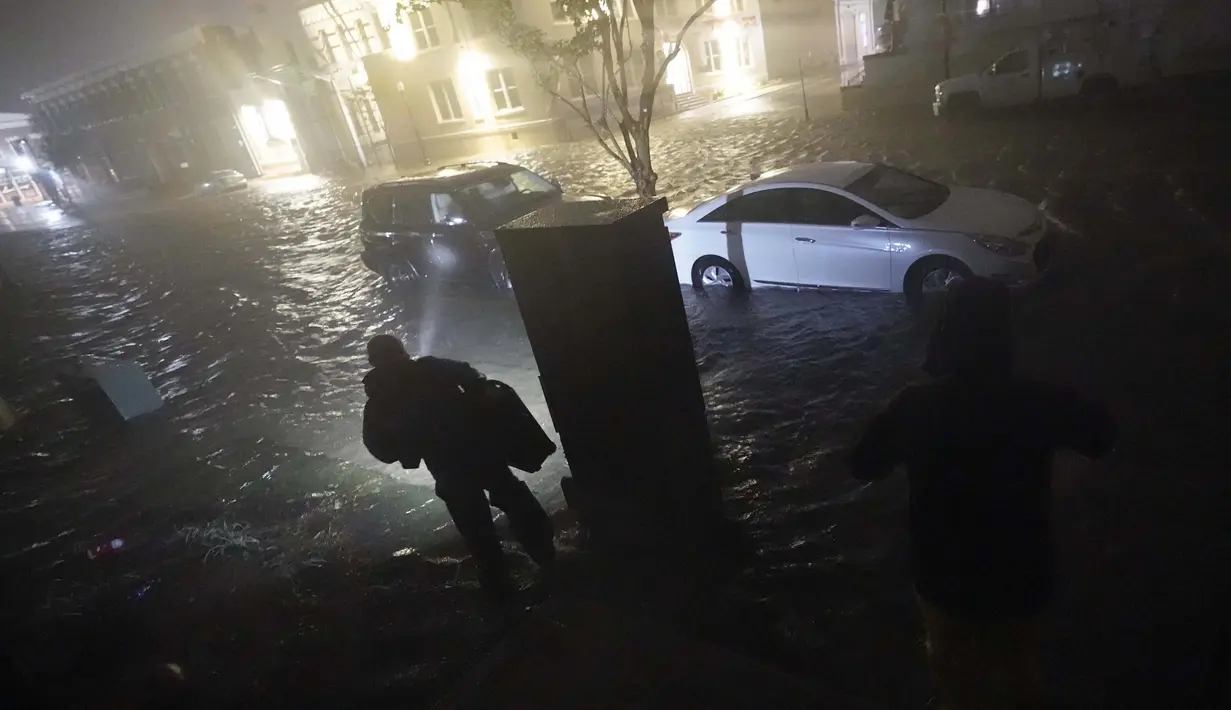 Orang-orang menggunakan senter saat mereka berjalan di jalan-jalan yang banjir untuk mencari kendaraan mereka di Pensacola, Florida, Rabu (16/9/2020). Badai Sally membuat pendaratan hari Rabu di dekat Gulf Shores, Alabama, sebagai badai Kategori 2. (AP Photo/Gerald Herbert)