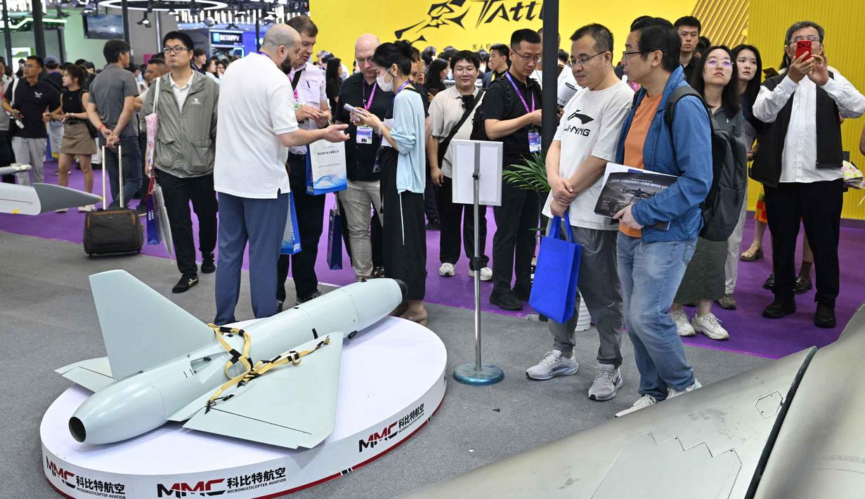 Pengunjung terlihat berdiri di samping model drone UAV Winged Tiger H1500 di stan Micro Multi Copter (MMC) selama Drone World Congress (DWC) di Shenzhen pada 21 Mei 2026. (HECTOR RETAMAL/AFP)