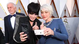 Aktris senior Helen Mirren melakukan wefie dengan sahabat sekaligus penyanyi Diane Warren di karpet merah Piala Oscar 2018, Los Angeles, Minggu (4/3). Acungan jari tengahnya tersebut menjadi perbincangan di internet. (Christopher Polk/GETTY IMAGES/AFP)