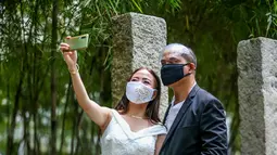 Pasangan berselfie dalam "pernikahan massal bermasker" di sebuah taman di Kota Makati, Filipina (15/12/2020). Pemerintah Filipina telah memberlakukan kebijakan untuk penggunaan masker di tengah kekhawatiran lonjakan kasus COVID-19 selama musim liburan. (Xinhua/Rouelle Umali)