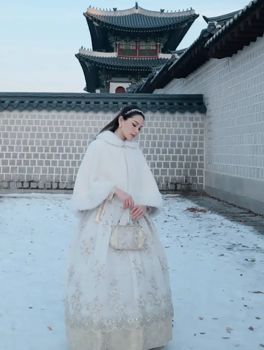 Ia nampak kenakan hanbok dress putih bermotif emas dilapisi coat berbulu warna putih [@alyssadaguise]