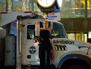 Penyanyi Lady Gaga berbusana serba hitam dan membawa bendera AS berunjuk rasa di depan Trump Tower, New York City, AS (9/11). Sebagai bentuk protesnya, Gaga mengangkat poster bertuliskan “Love Trumps Hate.”( AFP PHOTO/Dominick Reuter)