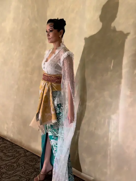 Titi Radjo Padmaja mengenakan kebaya putih lengan panjang transparan. Kebaya dari Denny Wirawan ini dipadukan obo kuning bermotif diatas belt songket, serta kain hijau bermotif silver. [@titiradjopadmaja]