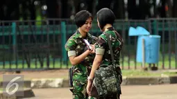 Prajurit wanita TNI melihat telepon genggam saat bersiaga di sekitar kawasan Stadion GBK Jakarta, Minggu (24/1/2016). TNI mengerahkan prajurit wanita untuk memberi rasa aman dan nyaman bagi para suporter perempuan. (Liputan6.com/Helmi Fithriansyah)