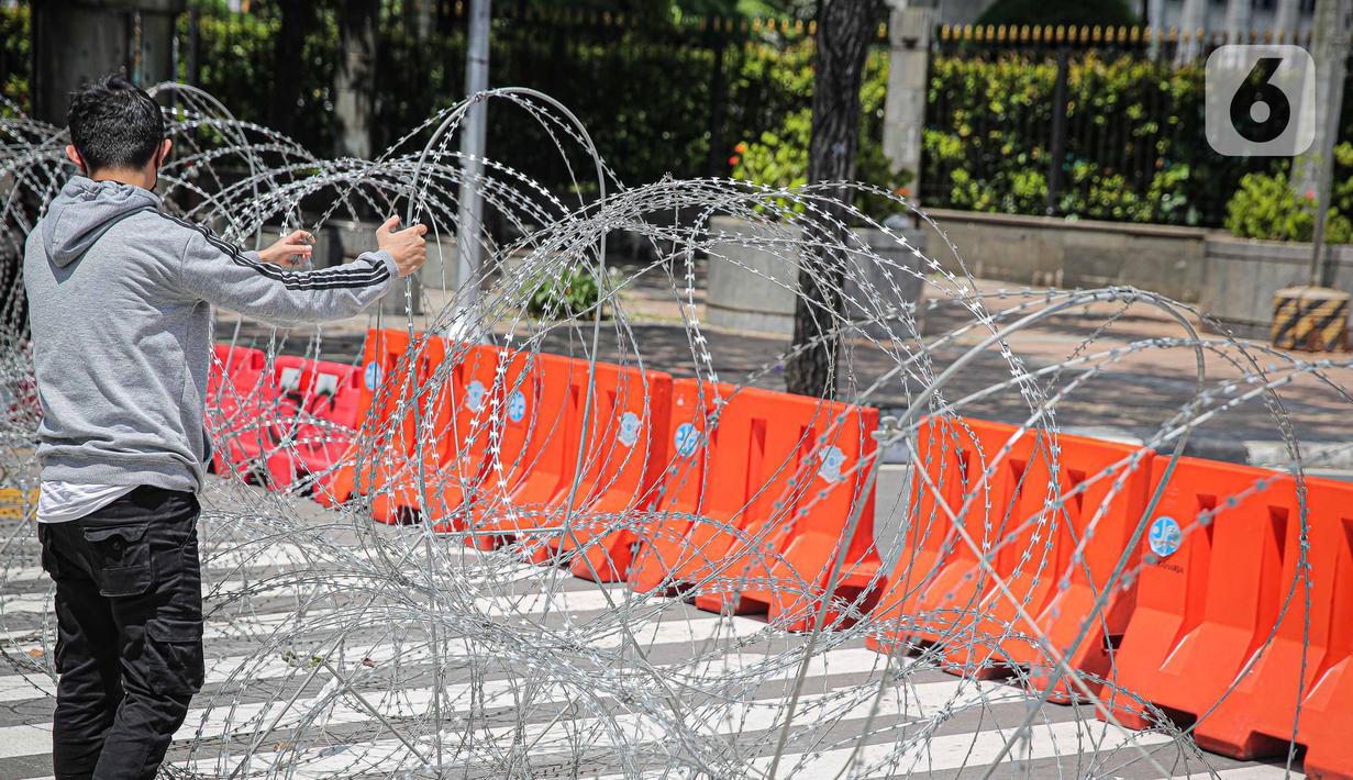 Seorang pria memegang kawat berduri di kawasan Jalan MH Thamrin, Jakarta, Kamis (2/12/2021). Polda Metro Jaya memasang barikade di sejumlah titik menuju kawasan Patung Kuda-Monumen Nasional (Monas) Jakarta Pusat guna mengantisipasi kerumunan massa aksi Reuni 212. (Liputan6.com/Faizal Fanani)