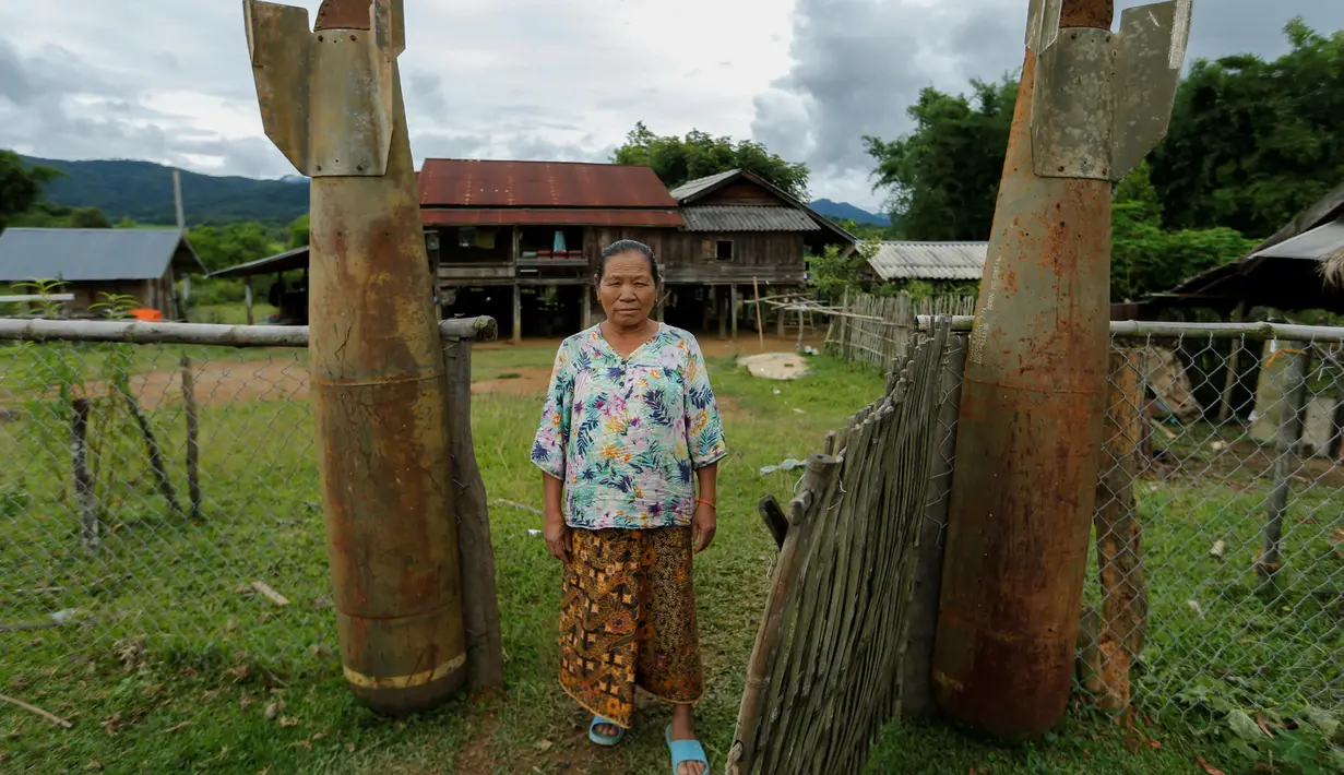Seorang wanita berpose di samping bom pintu masuk rumahnya yang dijatuhkan oleh pesawat Angkatan Udara AS selama Perang Vietnam, di Desa Ban Napia, Provinsi Xieng Khouang, Laos (03/9) (REUTERS/Jorge Silva)