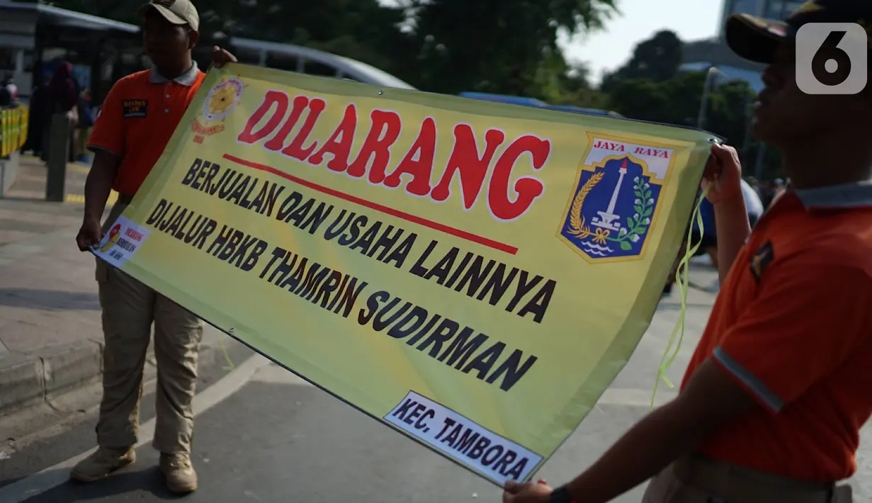 Petugas Satpol PP membentangkan spanduk larangan berjualan di jalur Hari Bebas Kendaraan Bermotor atau Car Free Day, Jakarta, Minggu (3/11/2019). Pemprov DKI melarang PKL berjualan di sepanjang jalur Car Free Day yang selama ini memenuhi badan jalan maupun trotoar. (Liputan6.com/Immanuel Antonius)
