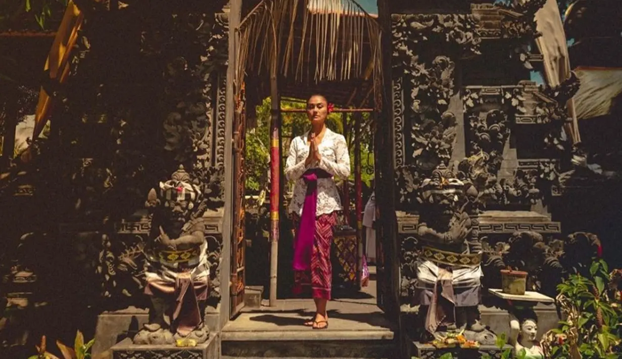 <p>Mempelajari budaya Bali saat di sana, pesona Agnez Mo ketika mengenakan busana adat Bali mencuri perhatian saat berpose di gapura. Ia mengenakan kebaya renda warna putih yang dipadukan dengan jarit warna ungu. (Liputan6.com/IG/@agnezmo)</p>