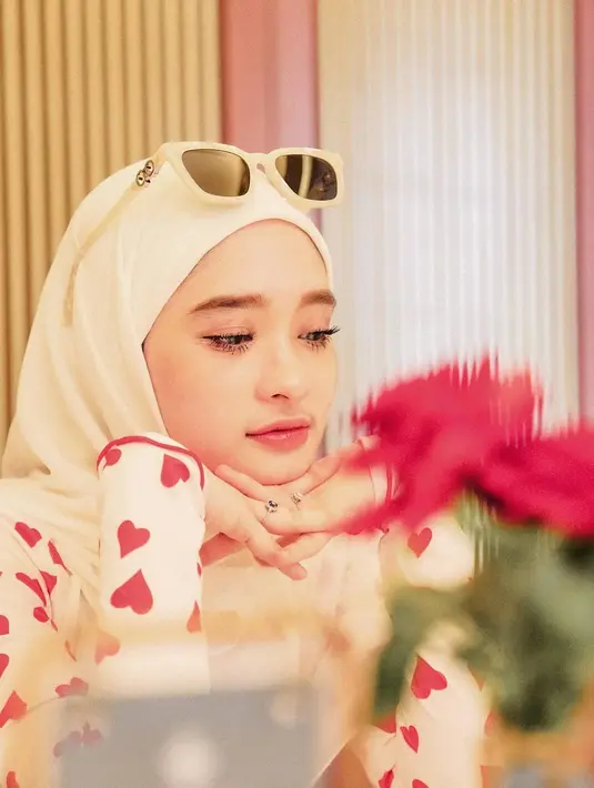 Inara Rusli pilih tampil manis kenakan sweater putih dengan monogram hati warna pink. Dipadukan dengan hijab dan kacamata putih. [@iinararusli_]