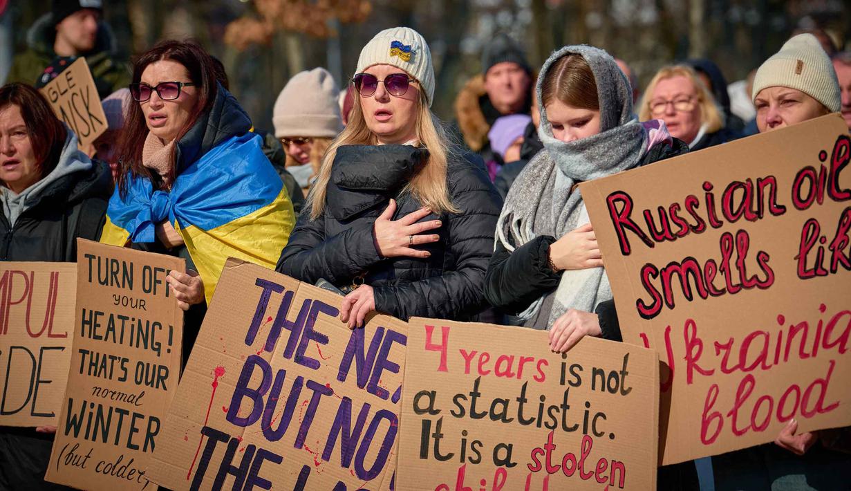 Anggota komunitas Ukraina, termasuk anak-anak dan pengungsi, berkumpul untuk menunjukkan solidaritas dan menuntut keadilan. Tampak dalam foto, orang-orang memegang spanduk saat anggota komunitas Ukraina menggelar protes untuk menandai tahun keempat sejak dimulainya invasi skala penuh Rusia ke Ukraina di Bukares, Rumania, Minggu 22 Februari 2026. (AP Photo/Vadim Ghirda)