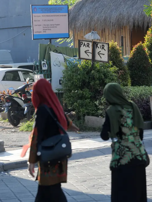 Dua wanita muslim berjalan melewati papan izin mendirikan bangunan (biru) di bekas lokasi bom Bali Sari Club di Kuta, Bali, Jumat (26/4). Perdana Menteri Australia Scott Morrison memprotes rencana pembangunan restoran di lahan bekas Sari Club yang merupakan lokasi pemboman Bali (SONNY TUMBELAKA/AFP)