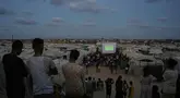 Warga Palestina menyaksikan siaran langsung pertandingan sepak bola Piala Dunia antara Spanyol dan Arab Saudi melalui layer lebar di Nuseirat, Jalur Gaza Tengah, Minggu 21 Juni 2026. (AP Photo/Abdel Kareem Hana)