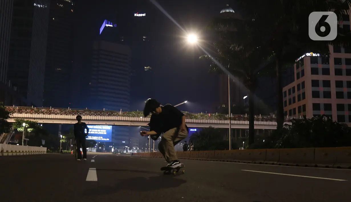 Warga bermain skateboard di jalan lengang kawasan Sudirman, Jakarta, Rabu (12/5/2021) malam. Polda Metro Jaya memberlakukan crowd free night untuk mencegah kerumunan takbir keliling di malam Idul Fitri 1442 yang berlaku mulai pukul 22:00 malam ini. (Liputan6.com/Herman Zakharia)
