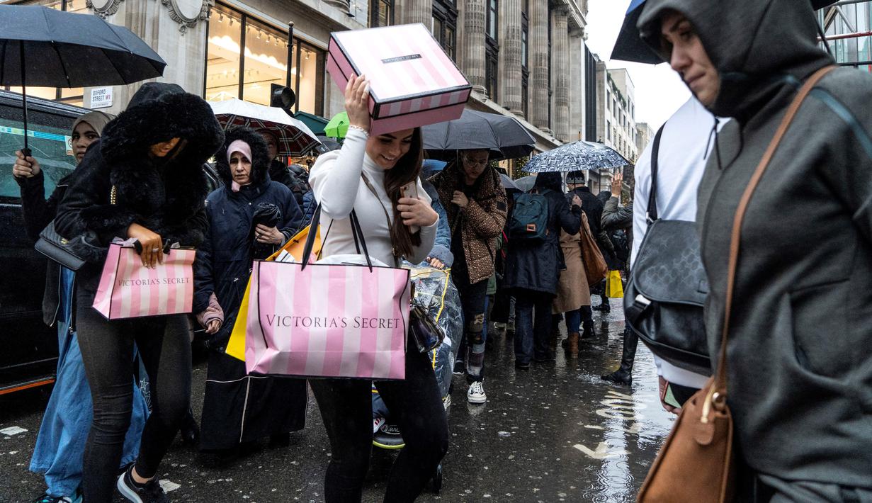 Pemburu diskon berlindung dari hujan dengan belanjaan mereka selama Boxing Day di London, Kamis (26/12/2019). Boxing Day merupakan tradisi hari belanja terbesar tahunan yang diperingati setiap 26 Desember atau sehari setelah Natal dan menjadi hari libur nasional di Inggris. (Niklas HALLE'N/AFP)
