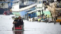 Warga menaiki becak untuk melintasi banjir rob di jalan Yos Sudarso Semarang di kawasan Pelabuhan Tanjung Emas (24/4). Banjir rob ini terjadi karena dipicu oleh salah satunya sistem drainase yang masih kurang baik. (Liputan6.com/Gholib)