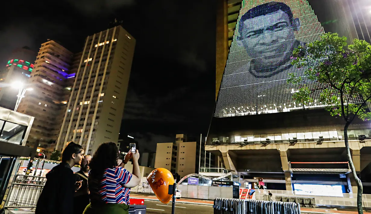 Seorang wanita mengambil gambar mendiang pemain sepak bola Pele yang ditampilkan pada Gedung Federasi Industri Sao Paulo di Sao Paulo, Brasil, 29 Desember 2022. Pele yang menghabiskan sebagian besar kariernya bersama Santos FC telah meninggal di Sao Paulo. (AP Photo/Marcelo Chello)