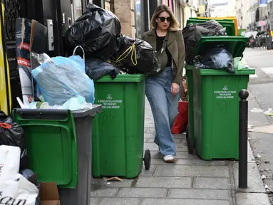 Seorang pejalan kaki berjalan di antara tempat sampah yang penuh di distrik ke-2 Paris saat petugas kebersihan mogok menentang reformasi pensiun, membuat banyak jalan di ibu kota penuh dengan sampah yang berbau busuk, Kamis (17/3/2023). (Photo by Bertrand GUAY / AFP)