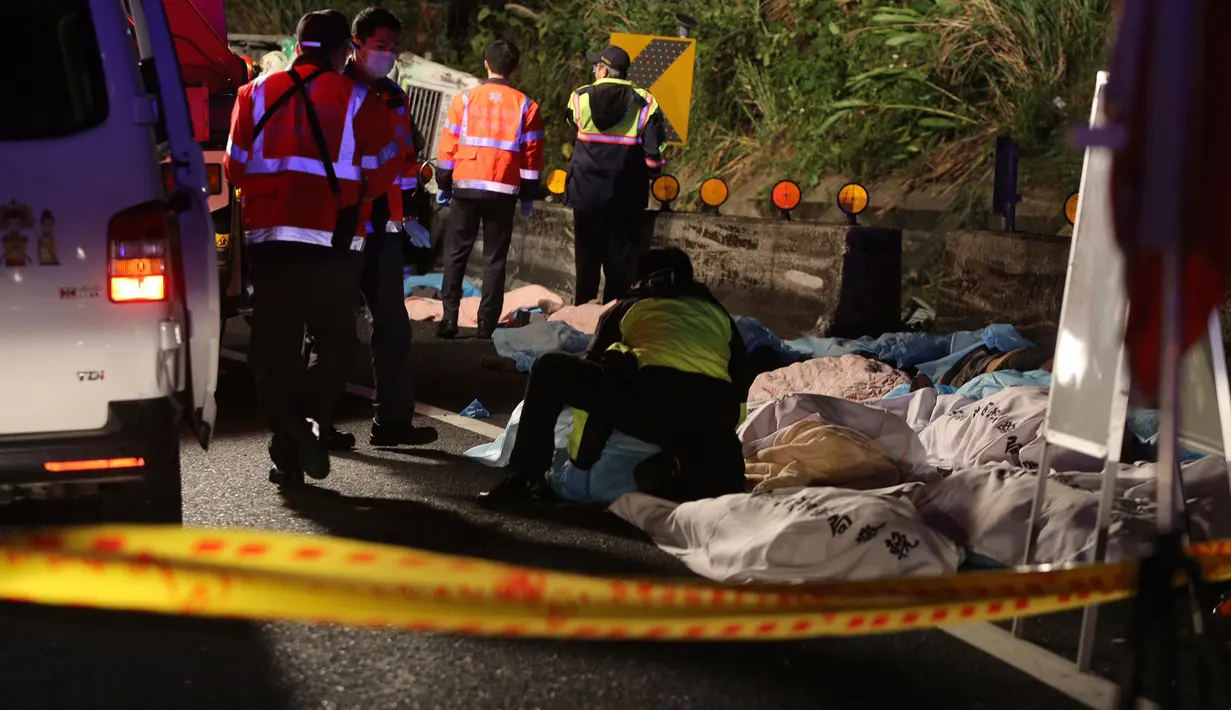 Petugas menutupi jasad penumpang yang tewas akibat bus wisata yang mereka tumpangi terbalik di ruas jalan dekat Taipe, ibu kota Taiwan, Selasa (14/2). Hingga saat ini kepolisian setempat masih melakukan investigasi terhadap kecelakaan tersebut. (AP Photo)