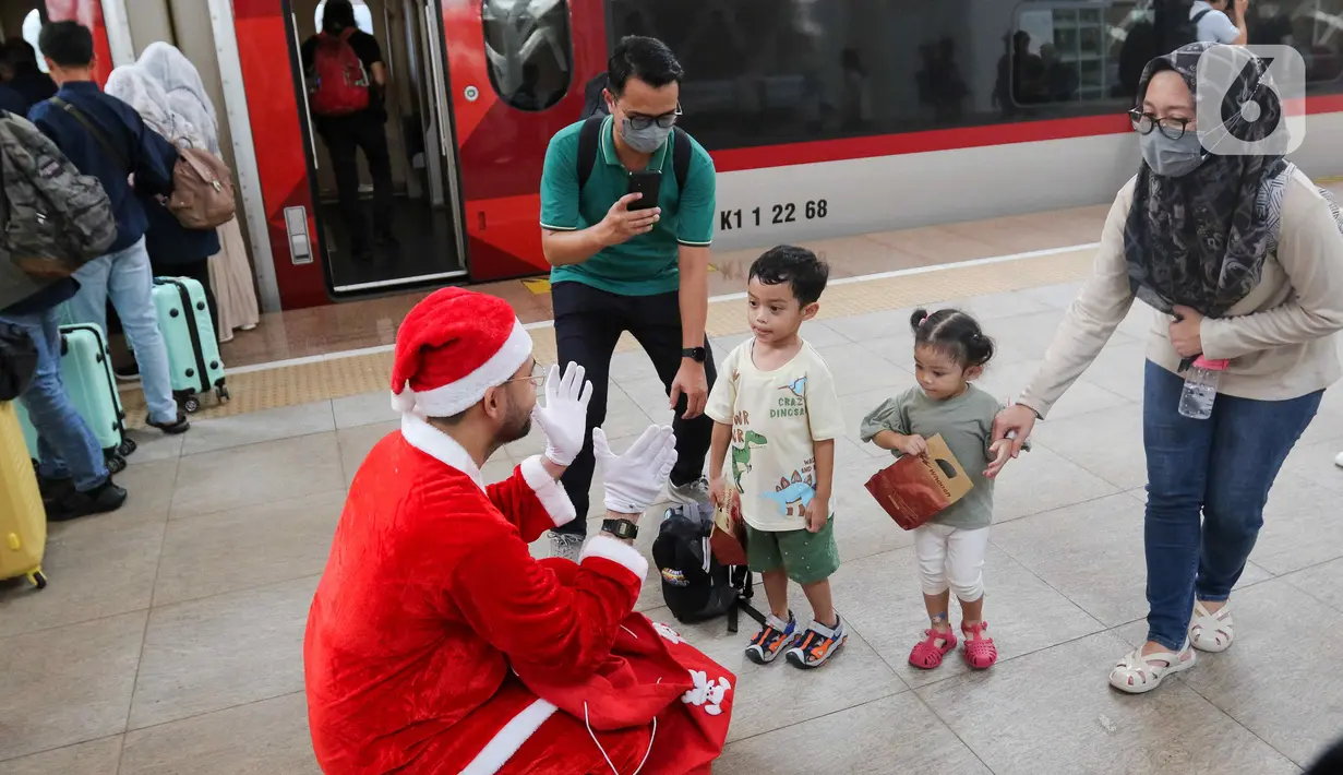 Pekerja yang mengenakan kostum Sinterklas berkomunikasi dengan anak-anak saat membagikan hadiah Natal kepada penumpang kereta cepat Whoosh. (Liputan6.com/Herman Zakharia)