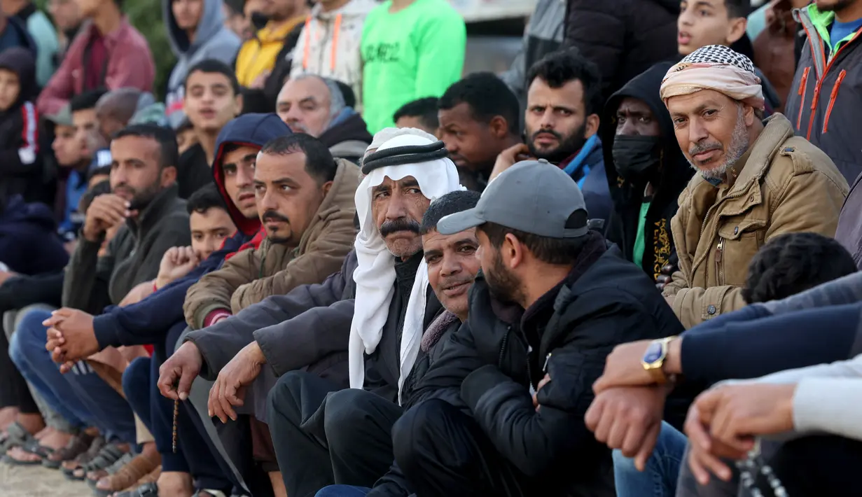 Warga Palestina menyaksikan pemuda bermain sepak bola di kamp pengungsi sebelum berbuka puasa selama bulan suci Ramadhan di Rafah, selatan Jalur Gaza (11/4/2022). Sepanjang bulan, umat Islam yang taat harus berpantang dari makanan dan minuman dari fajar hingga matahari terbenam. (AFP/Said Khatib)