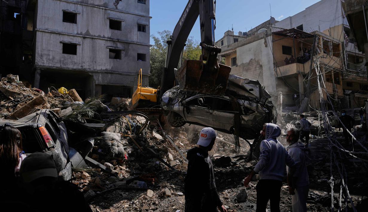 Pemerintah Lebanon menyatakan jumlah warga yang mengungsi telah melampaui 1,16 juta orang. Tampak dalam foto, sebuah ekskavator mengangkat mobil yang rusak dari reruntuhan sementara orang-orang berkumpul di lokasi serangan Israel pada Minggu 5 April 2026 terhadap sebuah bangunan di lingkungan Jnah, Beirut, Lebanon, Senin 6 April 2026. (AP Photo/Hassan Ammar)