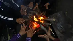 Sebuah keluarga duduk sekitar kayu bakar perapian rumah mereka saat cuaca dingin di daerah kumuh Kota Gaza, Palestina, 27 Januari 2022. (AP Photo/Hatem Moussa)