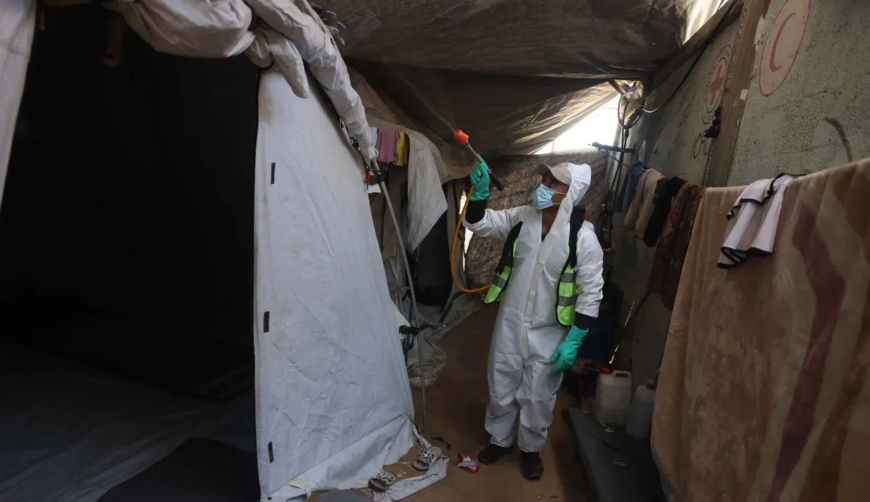 Seorang pengungsi Palestina menyemprotkan cairan disinfektan pada jalan setapak dan tenda-tenda untuk membasmi serangga dan hewan pengerat di kamp pengungsian Khan Yunis, Jalur Gaza Selatan pada Rabu 22 April 2026. Krisis kemanusiaan di Gaza kian memburuk. (Bashar Taleb/AFP)