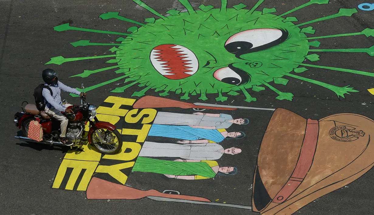 Pengendara motor melewati melewati grafiti virus corona yang dilukis di jalan selama penerapan lockdown nasional di Chennai, India, Senin (13/4/2020). Grafiti itu dibuat untuk meningkatkan kesadaran warga yang keluyuran keluar rumah saat lockdown karena pandemi virus corona. (Arun SANKAR/AFP)