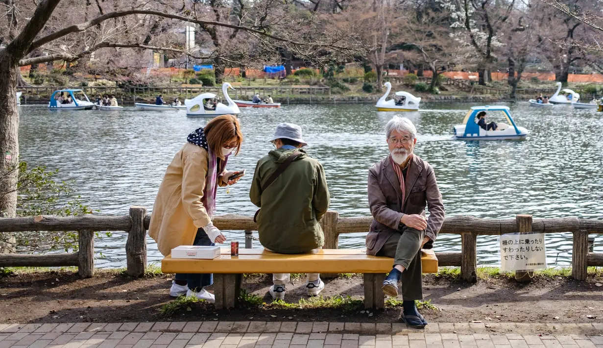 Orang-orang duduk di Taman Inokashira di Tokyo, Jepang, Senin (21/3/2022). Pada hari Minggu siang, setidaknya lima bunga telah mekar pada pohon yang menjadi patokan untuk varietas Somei-yoshino di Kuil Yasukuni di pusat Tokyo. (Philip FONG / AFP)