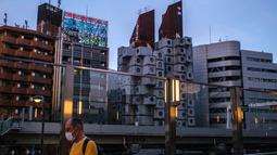 Seorang pria berjalan di sepanjang jembatan sebagai Landmark Nakagin Capsule Tower (tengah kanan), di distrik Ginza Tokyo, 6 April 2022. Menara yang selesai pada tahun 1972 dan dirancang oleh arsitek terkenal Kisho Kurokawa itu adalah sebuah landmark dari gerakan Metabolisme. (Philip FONG/AFP)
