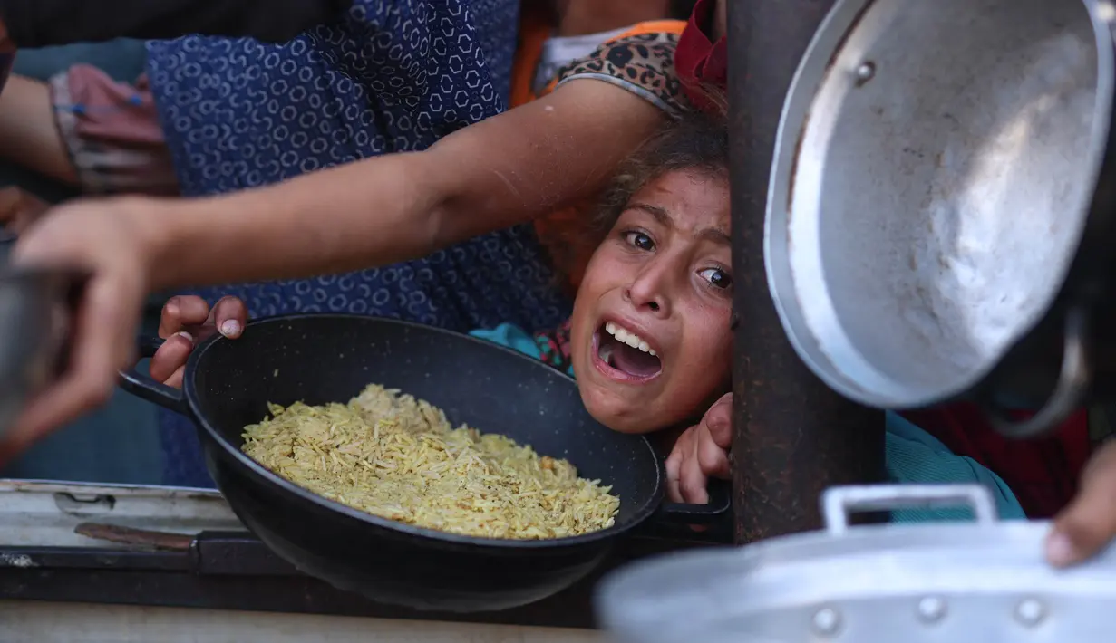 Sejumlah anak-anak ikut berdesakan sambil menggegam wadah untuk mendapatkan jatah makanan yang dibagikan. (BASHAR TALEB/AFP)
