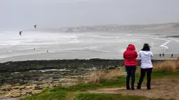 Dua wanita melihat peselancar layang selama cuaca badai di Teluk Wissant, Prancis utara (9/2/2020). Badai Ciara melanda sejumlah wilayah di Inggris dan benua Eropa bagian utara dengan hujan lebat disertai angin kencang pada Minggu 9 Februari 2020. (AFP Photo/Denis Charlet)