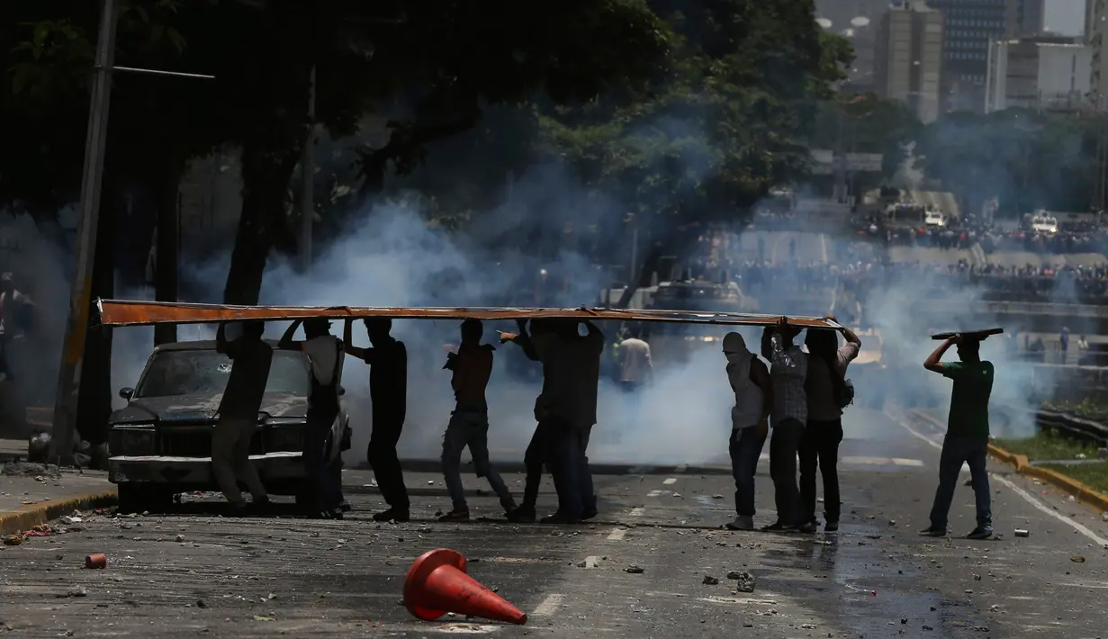 Para demonstran berlindung selama bentrokan antara anggota oposisi dan pasukan polisi di Caracas, Venezuela, (4/4). Mereka menuntut pemerintah menggembalikan kekuasaan kepada pihak opesisi. (AP Photo / Fernando Llano)